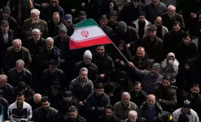 A man waves an Iranian flag as a crowd attends the funeral procession for senior Iranian military officials and civilians killed during the U.S.-Israel campaign in Tehran, Iran, Wednesday, March 11, 2026. (AP Photo/Vahid Salemi)