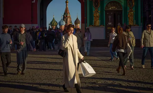 A woman speaking on the phone and carrying shopping bags leaves Red Square at sunset in Moscow, Monday, March 30, 2026, backdropped by the St. Basil's Cathedral. (AP Photo/Alexander Zemlianichenko)