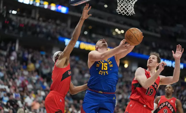 Denver Nuggets center Nikola Jokic drives to the basket between Toronto Raptors forward Brandon Ingram, left, and center Jakob Poeltl, right, in the first half of an NBA basketball game Friday, March 20, 2026, in Denver. (AP Photo/David Zalubowski)