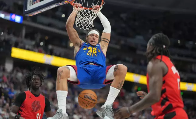 Denver Nuggets forward Aaron Gordon, center, hangs on the rim after dunking the ball for a basket between Portland Trail Blazers guards Sidy Cissoko, left, and Jrue Holiday in the second half of an NBA basketball game Sunday, March 22, 2026, in Denver. (AP Photo/David Zalubowski)