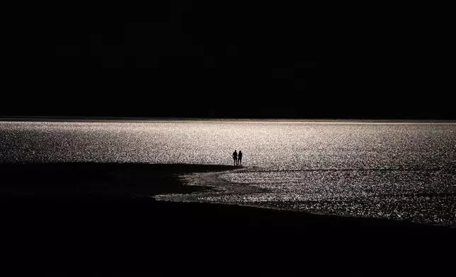 People stand along Lake Manly, an ephemeral lake at Badwater Basin, Saturday, March 7, 2026, in Death Valley National Park, Calif. (AP Photo/John Locher)