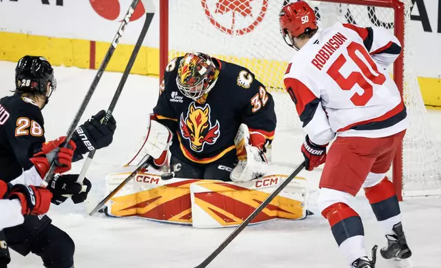 Carolina Hurricanes' Eric Robinson, right, has his shot stopped by Calgary Flames goalie Dustin Wolf during first period NHL hockey action in Calgary on Saturday, March 7, 2026.T (Jeff McIntosh/The Canadian Press via AP)