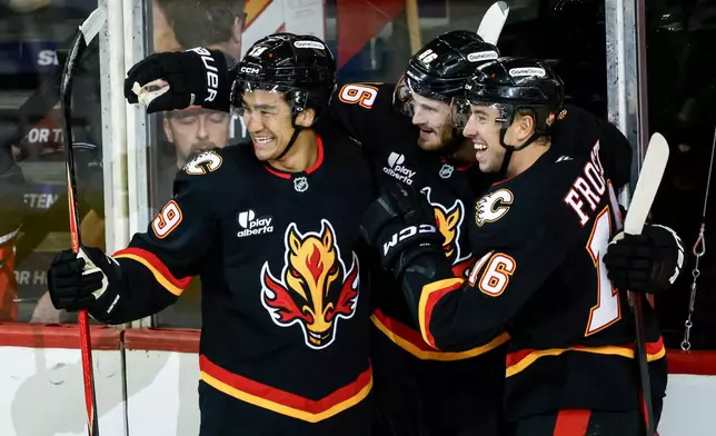 Calgary Flames' Joel Farabee, center, celebrates his goal with teammates Zayne Parekh, left, and Morgan Frost during the second period of an NHL hockey game against the Carolina Hurricanes in Calgary, Alberta, on Saturday, March 7, 2026. (Jeff McIntosh/The Canadian Press via AP)