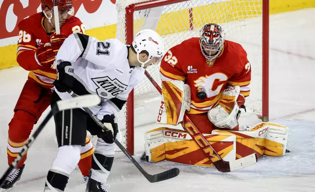 Los Angeles Kings' Scott Laughton, centre, has his shot blocked by Calgary Flames goalie Dustin Wolf, right, as Zach Whitecloud checks during the second period of an NHL hockey game in Calgary on Tuesday, March 24, 2026. (Jeff McIntosh/The Canadian Press via AP)