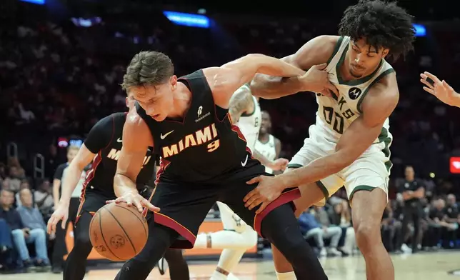 Milwaukee Bucks center Jericho Sims (00) and Miami Heat guard Pelle Larsson (9) go after a loose ball during the first half of an NBA basketball game Thursday, March 12, 2026, in Miami. (AP Photo/Marta Lavandier)