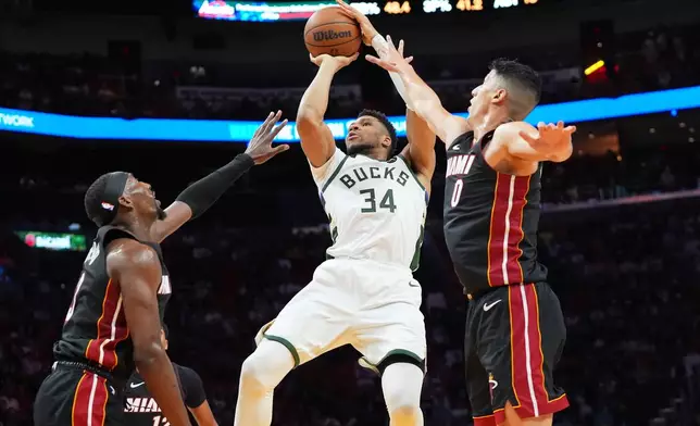 Milwaukee Bucks forward Giannis Antetokounmpo (34) aims to score as Miami Heat center Bam Adebayo (13) and Heat forward Simone Fontecchio (0) defend during the first half of an NBA basketball game Thursday, March 12, 2026, in Miami. (AP Photo/Marta Lavandier)