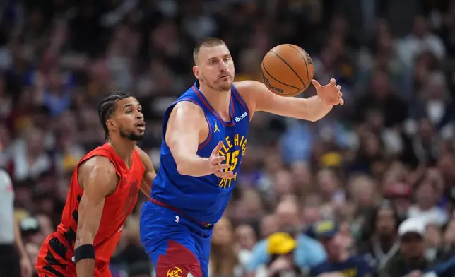 Denver Nuggets center Nikola Jokic, front, juggles the ball as Portland Trail Blazers forward Toumani Camara, left, defends in the first half of an NBA basketball game Sunday, March 22, 2026, in Denver. (AP Photo/David Zalubowski)
