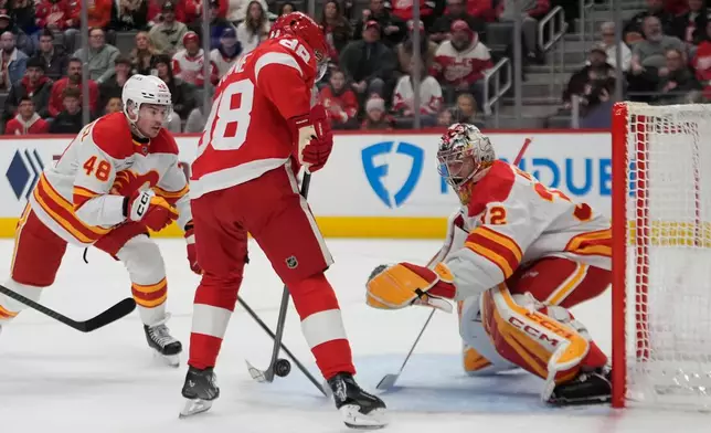 Calgary Flames goaltender Dustin Wolf (32) stops a Detroit Red Wings right wing Patrick Kane (88) shot as Hunter Brzustewicz (48) looks on in the first period of an NHL hockey game Monday, March 16, 2026, in Detroit. (AP Photo/Paul Sancya)