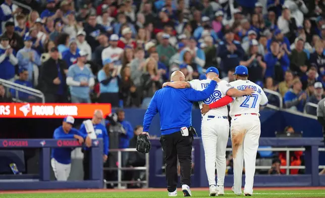Toronto Blue Jays catcher Alejandro Kirk, right, and a team trainer, left, help pitcher Mason Fluharty leave the game after he was hit by a second come-backer in the seventh inning of a baseball game against the Athletics in Toronto, Saturday, March 28, 2026. (Frank Gunn/The Canadian Press via AP)