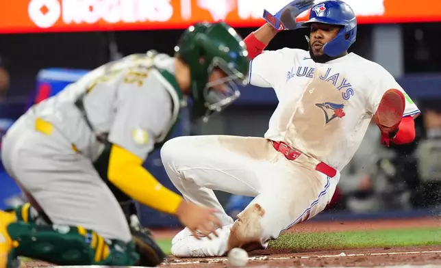 Toronto Blue Jays first baseman Vladimir Guerrero Jr. (27) slides into home plate to score in front of Athletics catcher Shea Langeliers (23) in the bottom of the sixth inning of a baseball game in Toronto on Saturday, March 28, 2026. (Frank Gunn/The Canadian Press via AP)
