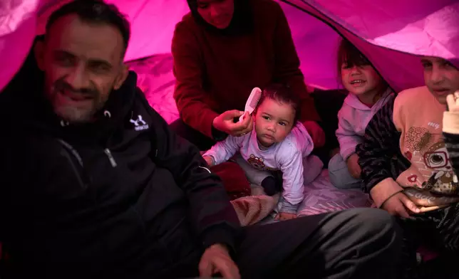 Members of the displaced Abd el-Hajj family, and two of their cousins, right, who fled Israeli strikes in southern Lebanon, sit inside a tent used as a shelter in Beirut, Lebanon, Wednesday, March 25, 2026. (AP Photo/Emilio Morenatti)