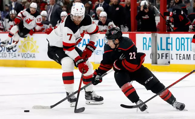 New Jersey Devils' Dougie Hamilton (7) takes the puck away from Carolina Hurricanes' Logan Stankoven (22) during the second period of an NHL hockey game in Raleigh, N.C., Saturday, March 28, 2026. (AP Photo/Karl DeBlaker)