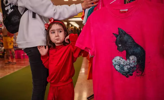 A child grimaces while looking at T-shirts displayed for sale at an international feline beauty competition, dubbed the Feline Oscars, featuring more than 200 cats, in Bucharest, Romania, Saturday, March 21, 2026. (AP Photo/Vadim Ghirda)