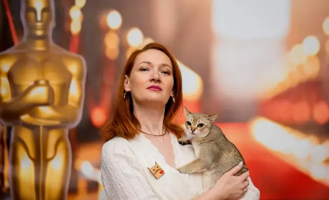 A woman poses with a Singapura cat in front of an Oscars themed photo backdrop during an international feline beauty competition, dubbed the Feline Oscars, featuring more than 200 cats in Bucharest, Romania, Saturday, March 21, 2026. (AP Photo/Andreea Alexandru)