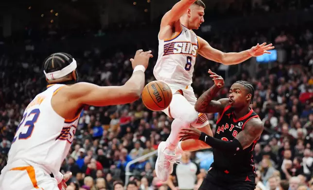 Toronto Raptors' Jamal Shead, right, passes the ball between Phoenix Suns' Jordan Goodwin, left, and Grayson Allen (8) during first-half NBA basketball game action in Toronto, Friday, March 13, 2026. (Frank Gunn/The Canadian Press via AP)