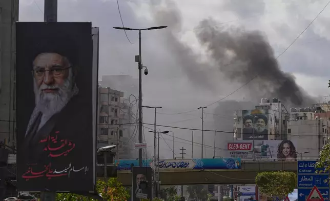 A portrait of Iran's late Supreme Leader Ayatollah Ali Khamenei, left, is seen, as smoke rises following an Israeli airstrike in Dahiyeh, Beirut's southern suburbs, Lebanon, Monday, March 30, 2026. (AP Photo/Hassan Ammar)