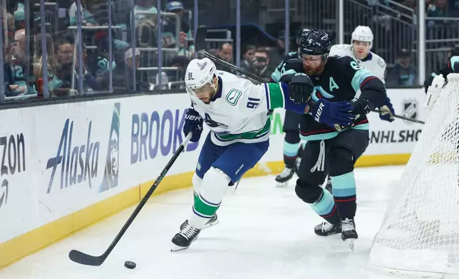 Vancouver Canucks left wing Evander Kane (91) moves the puck while defended by Seattle Kraken defenseman Adam Larsson (6) in the second period during an NHL hockey game Saturday, Feb. 28, 2026, in Seattle. (AP Photo/Kevin Ng)