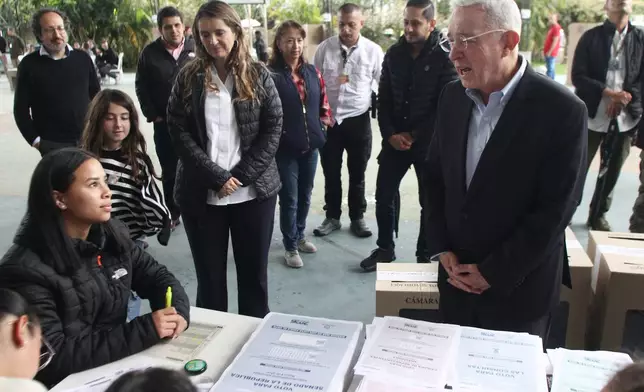 Former Colombian President Alvaro Uribe, right, talks to electoral official before voting during legislative elections in Rionegro, Colombia, Sunday, March 8, 2026. (AP Photo/Miguel Angel Lopez)