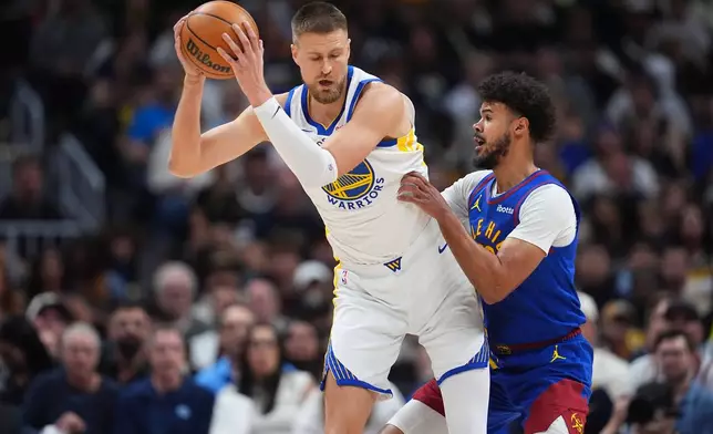 Golden State Warriors forward Kristaps Porziņģis, left, fields a pass as Denver Nuggets forward Cameron Johnson defends in the first half of an NBA basketball game Sunday, March 29, 2026, in Denver. (AP Photo/David Zalubowski)