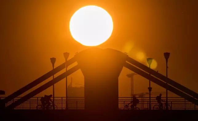 People ride their bicycles over a bridge in Frankfurt, Germany, as the sun rises on Wednesday, March 18, 2026. (AP Photo/Michael Probst)