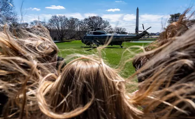 Hair from onlookers blows in the rotor wash as Marine One, with President Donald Trump aboard, lifts off from the South Lawn of the White House, Wednesday, March 18, 2026, in Washington. (AP Photo/Alex Brandon)
