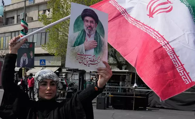 A woman displays a poster of the Iranian Supreme Leader Ayatollah Mojtaba Khamenei as she waves her country's flag during a campaign in support of the government at the Enqelab-e-Eslami, or Islamic Revolution, square in downtown Tehran, Iran, Saturday, March 14, 2026. (AP Photo/Vahid Salemi)
