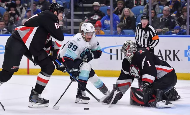 Seattle Kraken center Frederick Gaudreau, center, skates the puck toward the goal between Buffalo Sabres goalie Ukko-Pekka Luukkonen, right, and defenseman Logan Stanley, left, during the second period of an NHL hockey game Saturday, March 28, 2026, in Buffalo, N.Y. (AP Photo/Adrian Kraus)