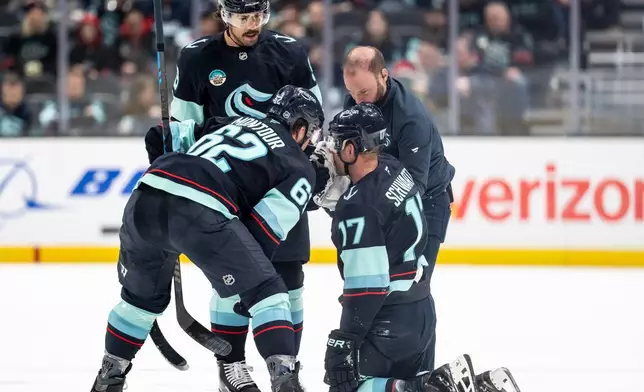 Seattle Kraken forward Jaden Schwartz (17) is tended to by team personnel and teammates defenseman Brandon Montour (62) and forward Chandler Stephenson (9) after a collision during the first periodof an NHL hockey game against the Ottawa Senators Saturday, March 7, 2026, in Seattle. (AP Photo/Stephen Brashear)