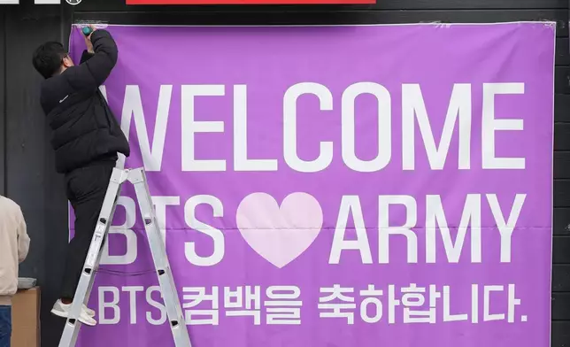 A man hangs a banner at a convenience store near the stage for a free concert by K-pop group BTS in Seoul, South Korea, March 18, 2026. (AP Photo/Lee Jin-man)