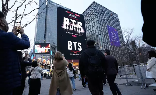 People take photos of a screen promoting a comeback concert of K-pop group BTS at Gwanghwamun Square in Seoul, Wednesday, March 18, 2026. (AP Photo/Ahn Young-joon)