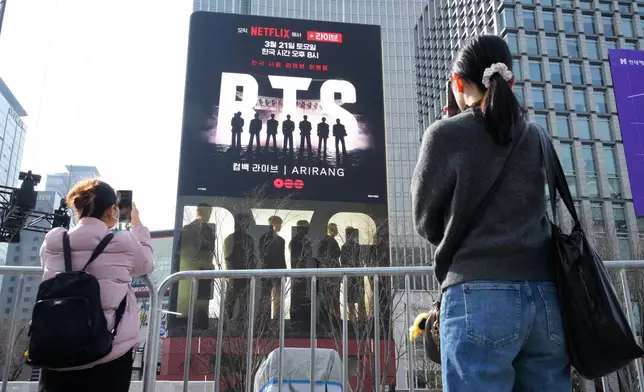 People take photos of a screen promoting a comeback concert of K-pop group BTS at Gwanghwamun Square in Seoul, Wednesday, March 18, 2026. (AP Photo/Ahn Young-joon)