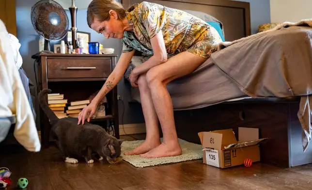 Mari Younger pets her cat Stella inside her converted hotel room where she lives after being displaced two years prior by the Maui fires, in Kihei, Hawaii, Wednesday, March 4, 2026. (AP Photo/Mengshin Lin)