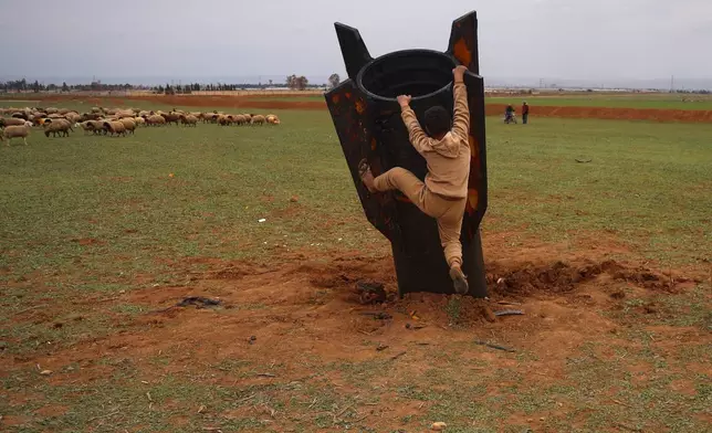 Exposing himself to the danger of unexploded ordnance, a boy tries to climb on an unexploded Iranian projectile that landed in an open field in the outskirts of Qamishli, eastern Syria, Wednesday, March 4, 2026.(AP Photo/Baderkhan Ahmad)