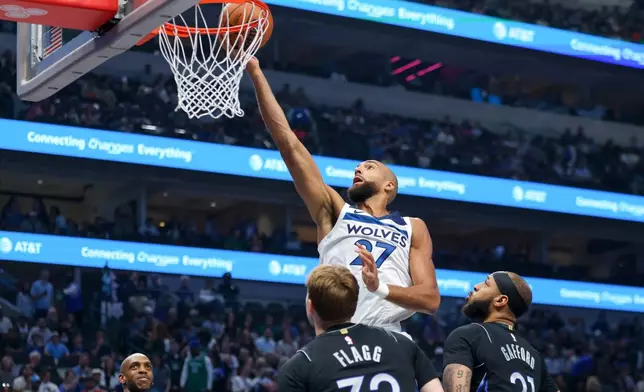 Minnesota Timberwolves center Rudy Gobert (27) scores past Dallas Mavericks forwards Daniel Gafford (21) and Cooper Flagg (32) in the first half of an NBA basketball game Monday, March 30, 2026, in Dallas. (AP Photo/Gareth Patterson)