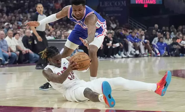 Philadelphia 76ers forward Justin Edwards, top, reaches for the ball held by Cleveland Cavaliers guard Keon Ellis, bottom, in the first half of an NBA basketball game in Cleveland, Monday, March 9, 2026. (AP Photo/Sue Ogrocki)