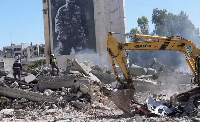 A giant poster shows the late Hezbollah military commander Imad Mughniyeh, while workers check a destroyed building that was hit by an Israeli airstrike in Nabatiyeh town, south Lebanon, Thursday, March 5, 2026. (AP Photo/Mohammed Zaatari)