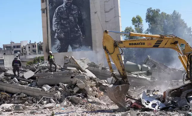 A giant poster shows the late Hezbollah military commander Imad Mughniyeh, while workers check a destroyed building that was hit by an Israeli airstrike in Nabatiyeh town, south Lebanon, Thursday, March 5, 2026. (AP Photo/Mohammed Zaatari)