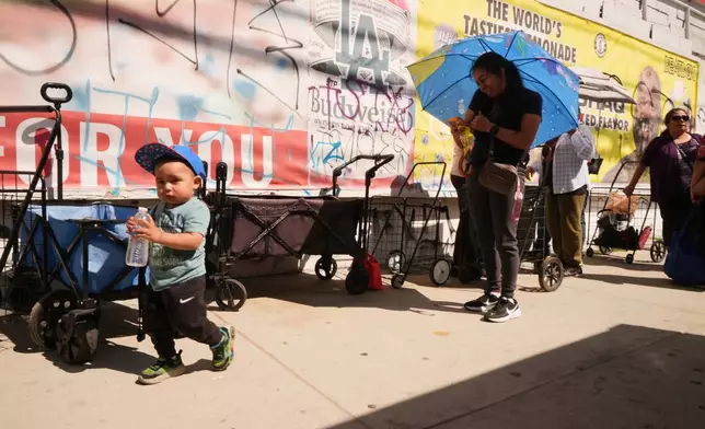 People cover themselves from the heat with umbrellas while waiting at a food distribution site Wednesday, March 11, 2026, in Los Angeles. (AP Photo/Damian Dovarganes)