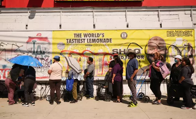 People cover themselves from the heat with umbrellas while waiting at a food distribution site Wednesday, March 11, 2026, in Los Angeles. (AP Photo/Damian Dovarganes)