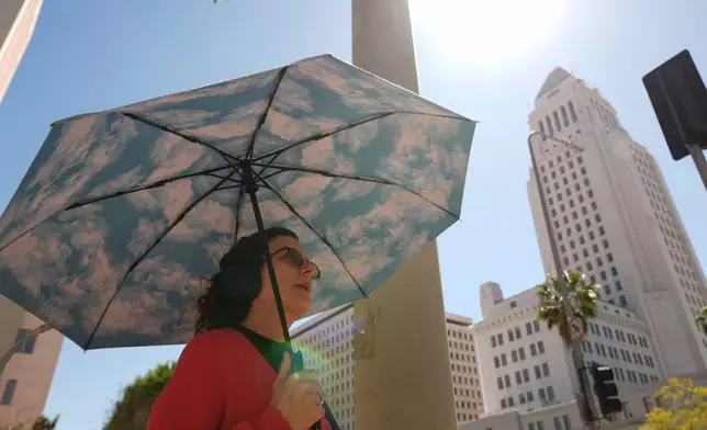 A pedestrian holds a cloud themed umbrella under a sunny day next to Los Angeles City Hall in Los Angeles Thursday, March. 12, 2026. (AP Photo/Damian Dovarganes)