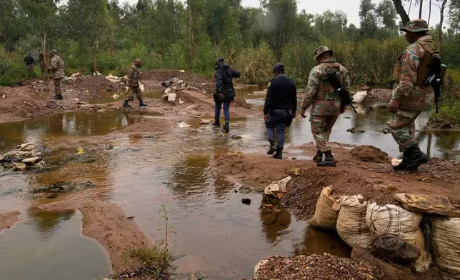 South African National Defense Force soldiers and police officers cross a water stream used by illegal miners, during a patrol in Randfontein, in Johannesburg, South Africa, Thursday, March 12, 2026. (AP Photo/Themba Hadebe)