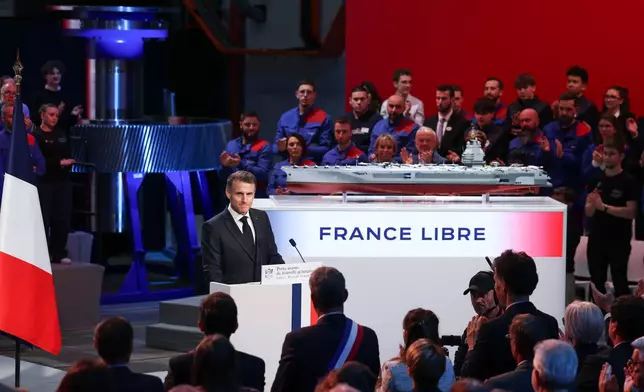 French President Emmanuel Macron stands next to the model of a ship named "France Libre", as he delivers a speech during his visit to the construction site of Naval Group Nantes-Indret, where the next generation of French aircraft carrier is under construction, in Indret, France, Wednesday, March 18, 2026. (Gonzalo Fuentes/Pool Photo via AP)