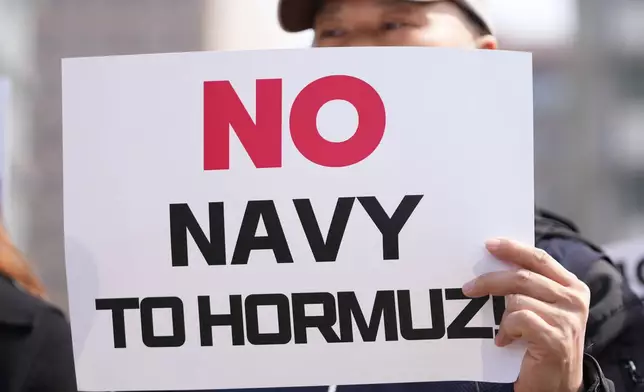 A protester holds a sign against Donald Trump's demands to multiple countries to send warships to keep the Strait of Hormuz open, near the U.S. Embassy in Seoul, South Korea, Monday, March 16, 2026. (AP Photo/Lee Jin-man)