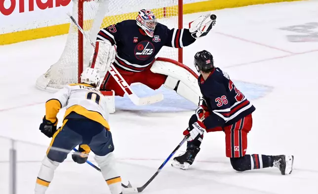 Winnipeg Jets goaltender Connor Hellebuyck (37) makes a save on Nashville Predators' Filip Forsberg (9) as Morgan Barron (36) defends during the overtime period of their NHL hockey game in Winnipeg, Tuesday March 17, 2026. (Fred Greenslade/The Canadian Press via AP)