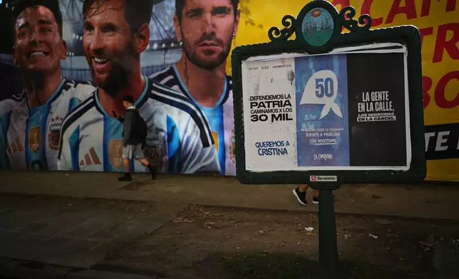 A man walks past a painting depicting Argentina's national soccer team players Lionel Messi, center, Julian Alvarez, left, and Rodrigo De Paul near a banner reading in Spanish, "Let’s defend the homeland by marching for the 30,000" referring to a number people disappeared during the military dictatorship, on the anniversary of the military coup that brought the military regime to power, in Buenos Aires, Argentina, Tuesday, March 24, 2026. (AP Photo/Rodrigo Abd)