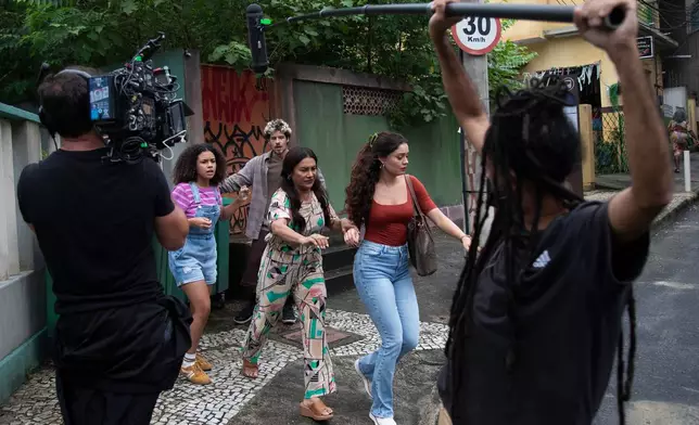 Actors Alana Cabral, behind left, Dira Paes, center, Sophie Charlotte, behind right, and Paulo Mendes, behind everyone, take part in the filming of the soap opera "Três Garças" at a TV Globo set in Rio de Janeiro, Thursday, March 12, 2026. (AP Photo/Bruna Prado)