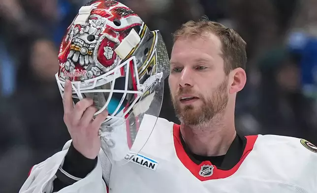 Ottawa Senators goalie James Reimer checks the inside his mask during a stoppage in play during the third period of an NHL hockey game against the Vancouver Canucks, in Vancouver, on Monday, March 9, 2026. (Darryl Dyck/The Canadian Press via AP)