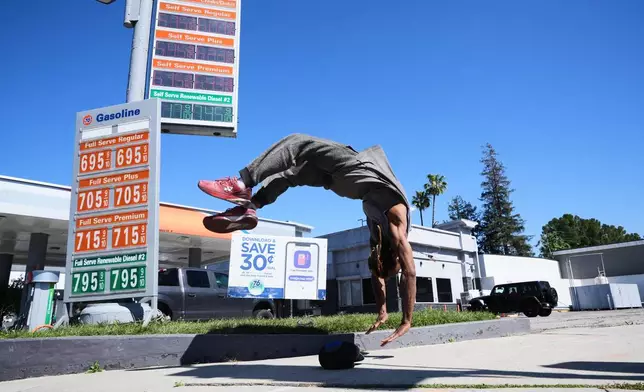 Marcus Hopkins, a street performer, does a backflip in front of advertised gas prices Monday, March 9, 2026, in Los Angeles. (AP Photo/Damian Dovarganes)