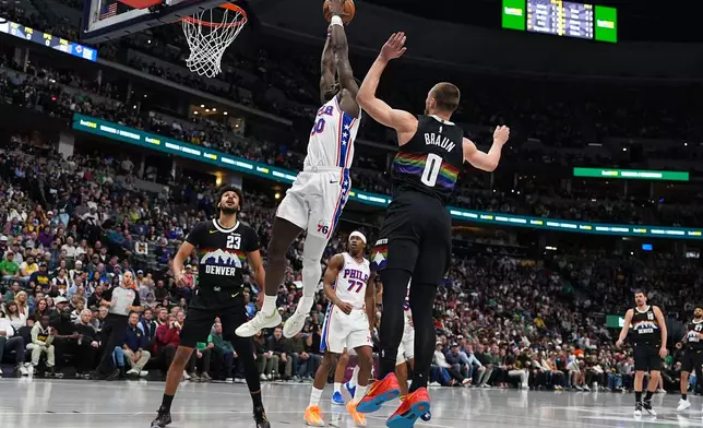 Philadelphia 76ers forward Adem Bona drives between Denver Nuggets forward Cameron Johnson, back, and guard Christian Braun, front, to dunk the ball for a basket in the first half of an NBA basketball game Tuesday, March 17, 2026, in Denver. (AP Photo/David Zalubowski)