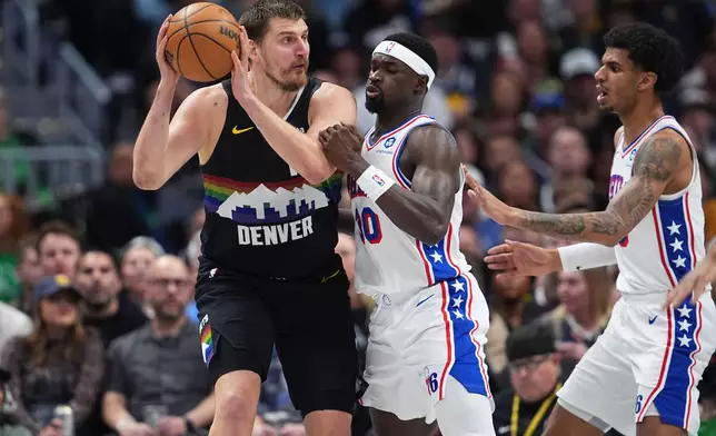 Denver Nuggets center Nikola Jokić, left, looks to pass the ball as Philadelphia 76ers forwards Adem Bona and Dominick Barlow, right, defend in the first half of an NBA basketball game Tuesday, March 17, 2026, in Denver. (AP Photo/David Zalubowski)